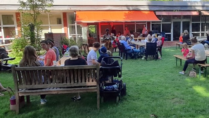 Freilufttreffen mit Personen, die auf Bänken und Tischen in einem schattigen Bereich eines Gemeinschaftsgartens sitzen.