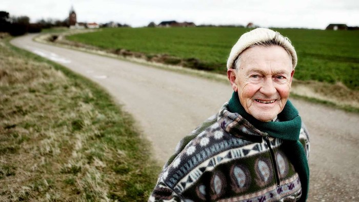 En ældre dame smiler varmt, mens hun står på en landevej.