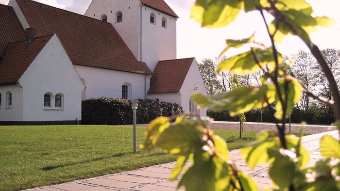 En hvid kirke med røde tag og en grøn have foran
