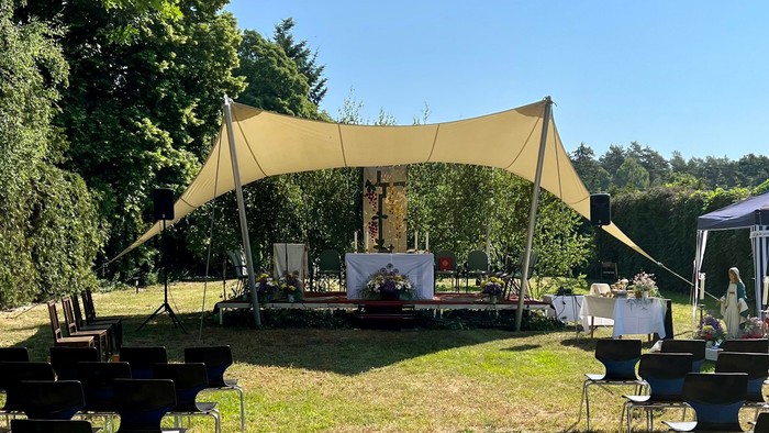 Im Garten sitzen Menschen unter einem Zelt an Tischen.