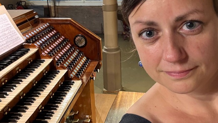En person står ved siden af et stort pibeorgel med et fokuseret, tilfreds udtryk.