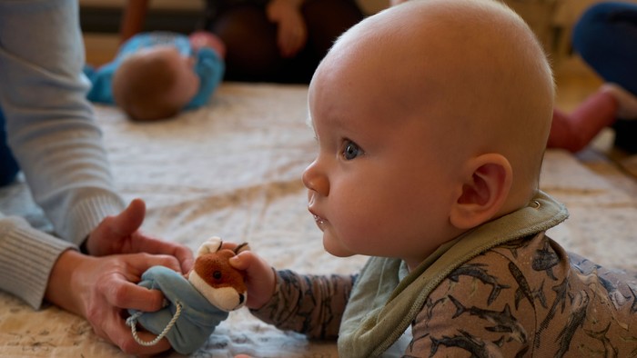 Et spæd barn ligger på en blomsterbetaget matras og holder en blå legetøj.