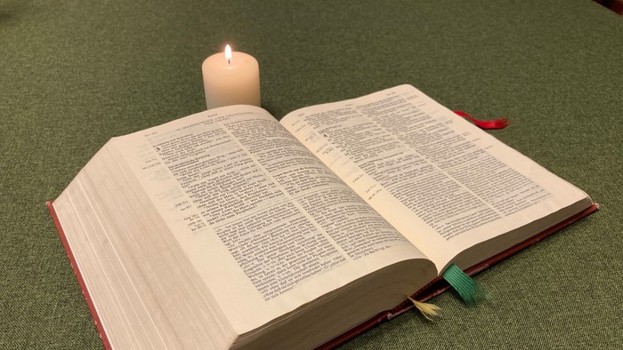 Offenes Buch mit brennender Kerze darauf auf grüner Oberfläche