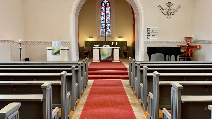 Die Kirche mit einem roten Teppich und Holzbänken, einem Altar und einem Kreuz.
