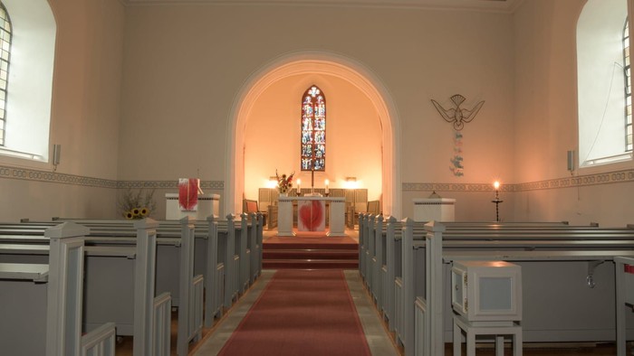 Die Kirche mit weißen Bänken und einem Altar mit Kreuz.
