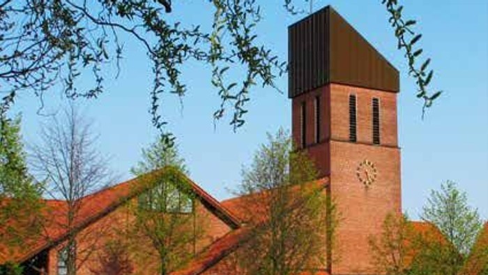 Moderne Backsteinkirche mit hohem Turm, umgeben von blühenden Bäumen und einem gepflegten Rasen.