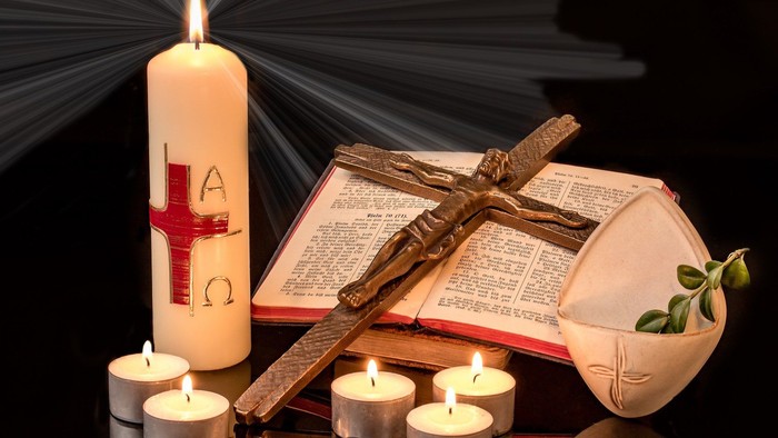 Brennende Kerzen, Kreuz und offenes Buch auf schwarzem Hintergrund