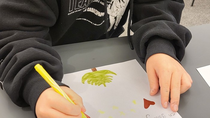 En dreng sidder ved et bord og tegner på et papir.