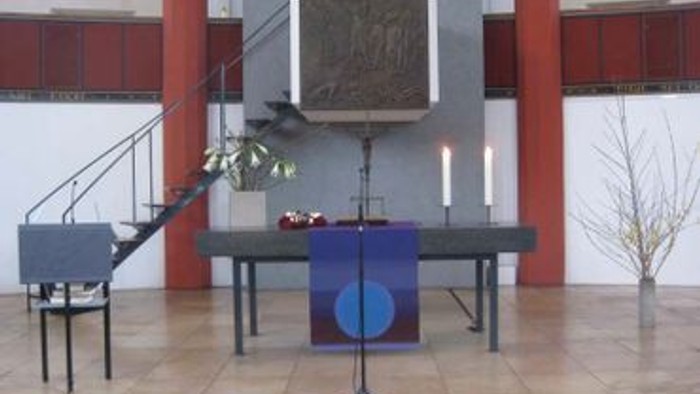Ein moderner Altar in einer Kirche mit Tisch, Kerzen und einem Bild.