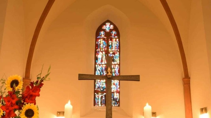 In der Kirche: Altar mit Kreuz, Kerzen und Blumen vor buntem Fenster