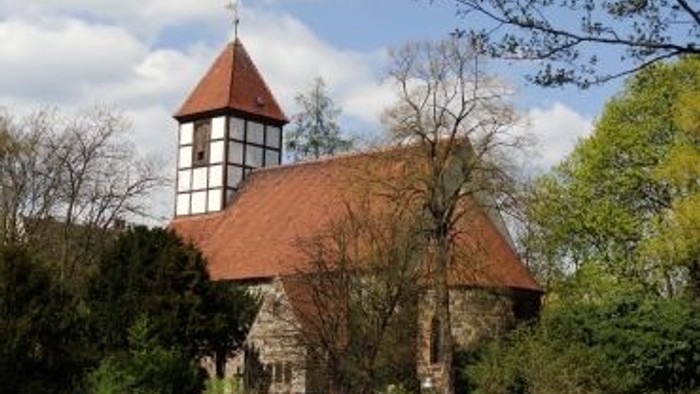 Kleine Kirche mit rotem Dach und Turm, umgeben von Bäumen und Büschen