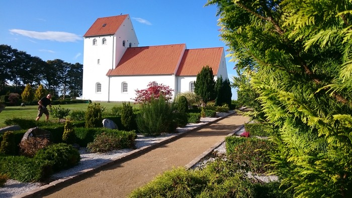 En smuk hvid kirke med rødt tag og en grøn have.