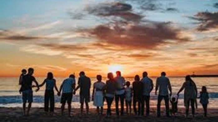 Eine Familie steht bei Sonnenuntergang Hand in Hand am Strand und genießt die goldene Stunde am Meer.