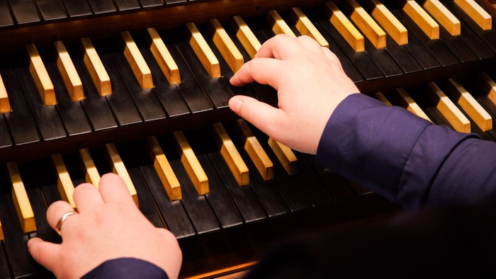 Ein Blick über die Schulter einer Organistin auf die schwarzen Manuale einer Orgel