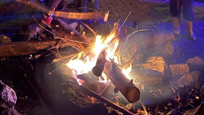 Eine Gruppe von Menschen steht um ein Lagerfeuer und genießt die warme Atmosphäre.