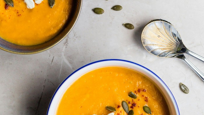 Warme, cremige Kürbissuppe, garniert mit zerbröckeltem Käse, Kürbiskernen und frischen Kräutern auf einer Marmorfläche.