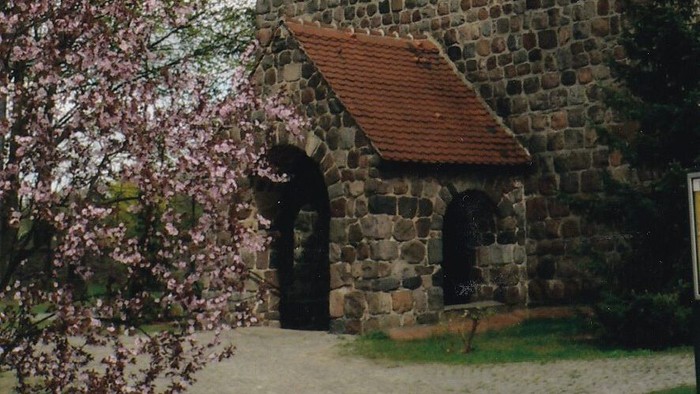 Eingang der Dorfkirche mit blühendem Strauch auf der linken Seite des Bildes