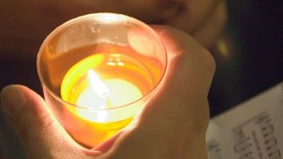 Eine Hand hält ein brennendes Teelicht.