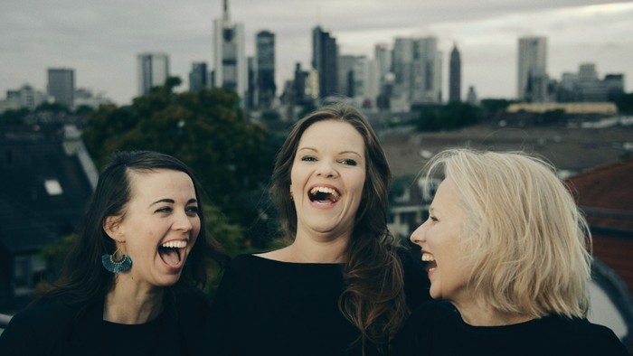 Drei Frauen lachen gemeinsam vor einer Stadtskyline.