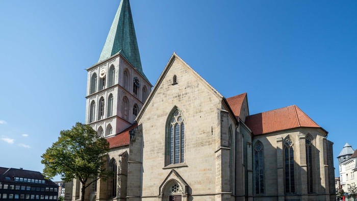 Große Kirche mit hohem Turmspitz und rotem Dach vor blauem Himmel.