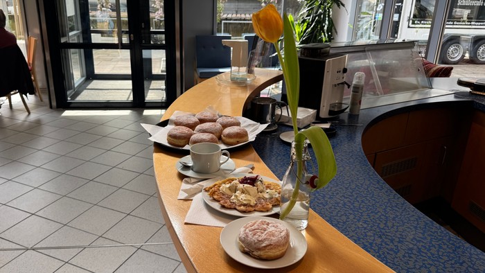 Ein gemütlicher Café-Tresen präsentiert Gebäck, Donuts und eine Blumenarrangement, während eine Person in der Nähe sitzt.