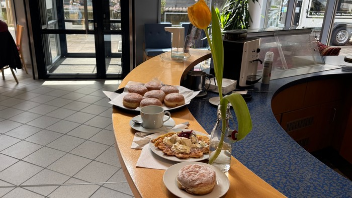 Ein gemütlicher Café-Tresen präsentiert Gebäck, Donuts und eine Blumenarrangement, während eine Person in der Nähe sitzt.