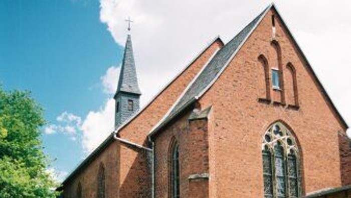 Ein rotes Backsteingebäude mit spitzen Fenstern und einem Turm, umgeben von grünem Gras und Blumen.