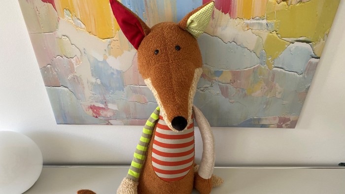 Ein Stofftier Fuchs sitzt vor einem farbenfrohen Gemälde.
