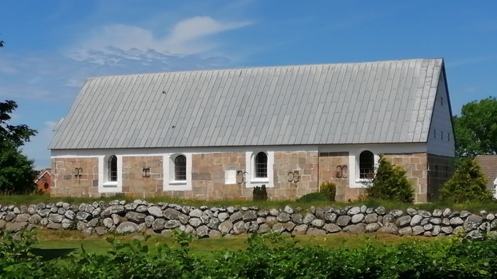 Stenum Kirke fra sydsiden. Kirkediget, grønne planter foran. Blå himmel