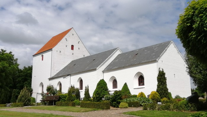 Thise Kirke fra sydsiden, grønne planter på kirkegården, syker på himmlen