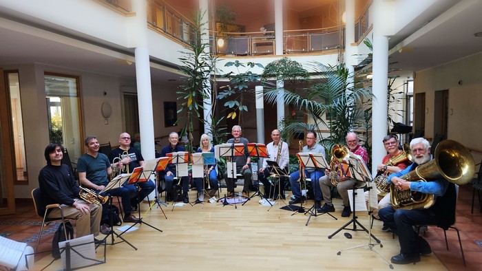 Eine Gruppe von Musiker:innen, die Blechblasinstrumente in einem hellen, Innenraum-Aufführungsbereich spielen.
