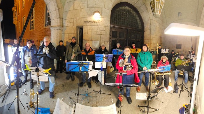 Eine Gruppe von Musikern proben in einem großen, hell erleuchteten Raum mit hohen Decken und Bögen.