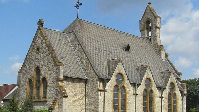 Historische Steinkirche mit steilem Dach, spitzen Fenstern und einem kleinen Glockenturm unter klarem Himmel.