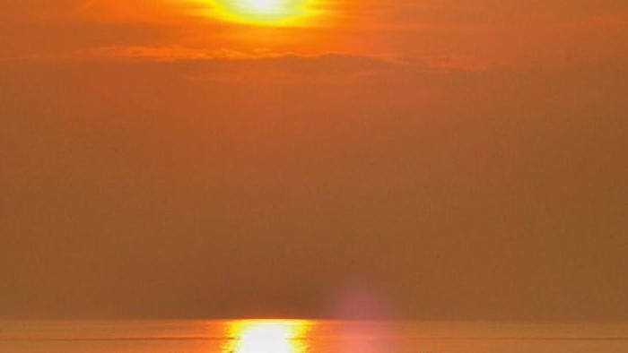 Ein friedlicher Sonnenuntergang über ruhigem Wasser mit einem einsamen Boot, das goldenes Licht widerspiegelt.