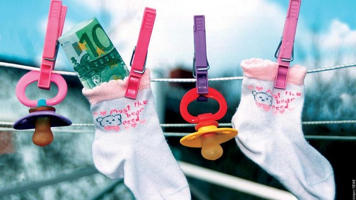 Bunte Babysöckchen mit Schnullern und Euro-Scheinen, die mit dekorativen Klammern an einer Wäscheleine aufgehängt sind.