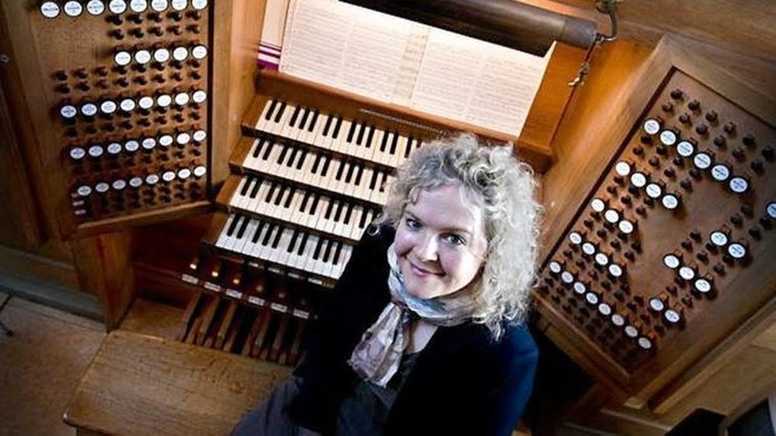 Kvinde sitter ved et orgel og smiler.