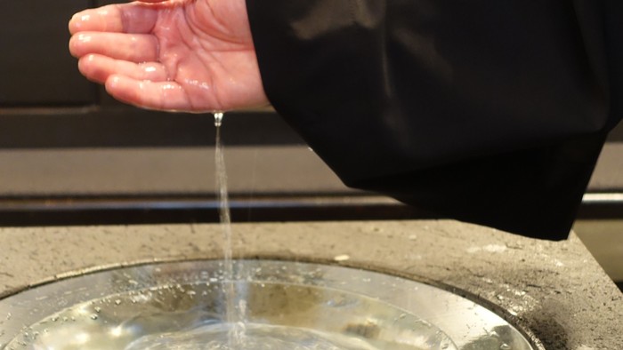 Person wäscht sich die Hände über einer Metallschale