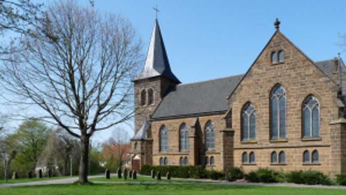 Ein Kirchengebäude mit hohem Turm und spitzen Fenstern steht auf einem grünen Rasen.