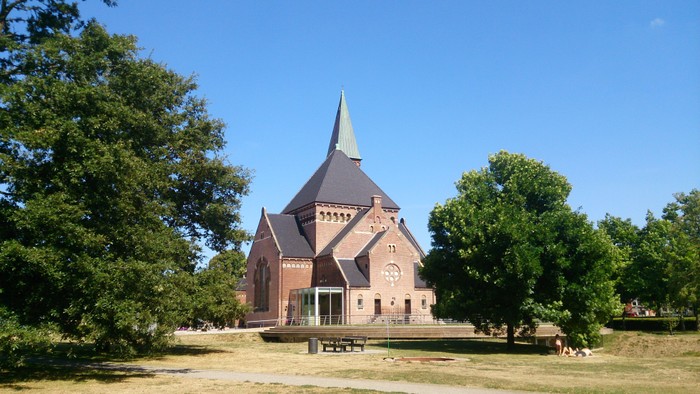 En rød kirke med spir med træer og klar himmel i baggrunden
