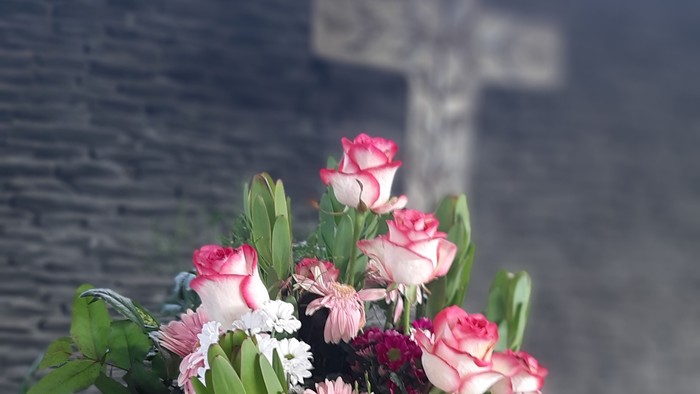 Blumenstrauß in Vase vor Kreuz an der Wand