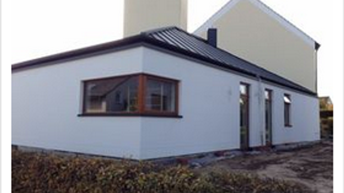 Das Bild zeigt ein modernes, weißes Haus mit großen Fenstern und einem Kamin.