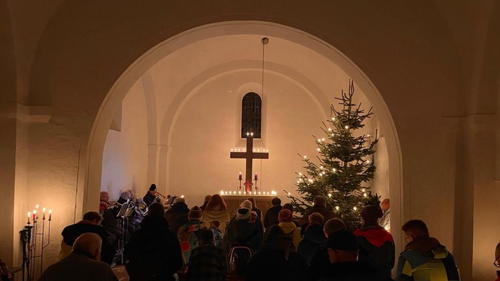 Ein festlicher Weihnachtsgottesdienst mit Teilnehmern, die sich um einen geschmückten Baum und Altar versammelt haben und Kerzen halten.