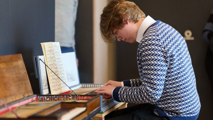 Unge mand spiller på et keyboard, mens han koncentreret læser nodenoter.