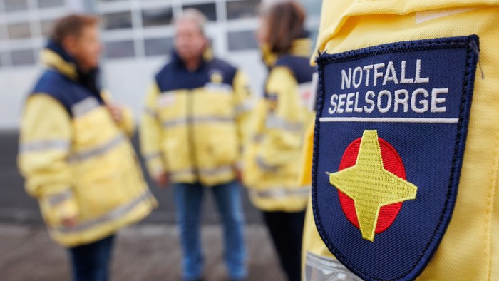 Drei Personen in gelben Jacken mit Notfall Seelsorge Abzeichen.