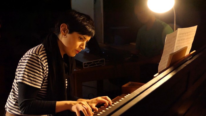 En person spiller på et keyboard med noder, der er oplyst af en fokuseret skrivebordslampe.