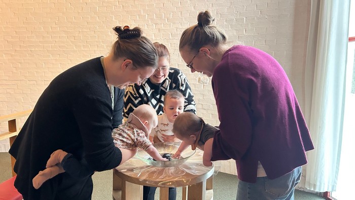 En gruppe voksne og babyer deltager i en hands-on sanseaktivitet ved et bord sammen.