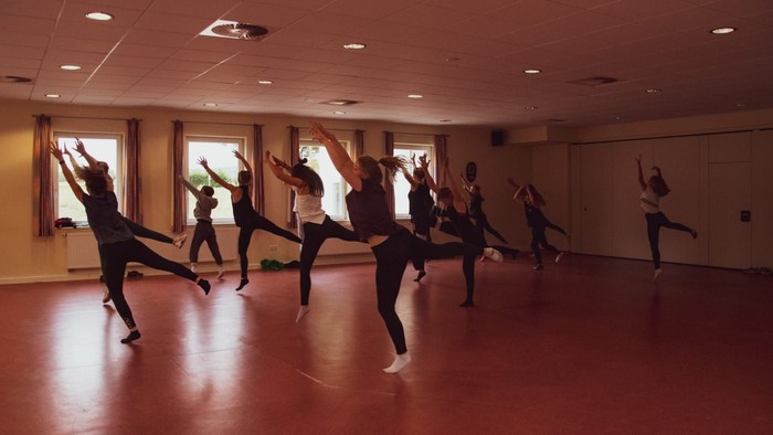 Eine Gruppe von Tänzern führt moderne Tanzbewegungen in einem gut beleuchteten Studio aus.