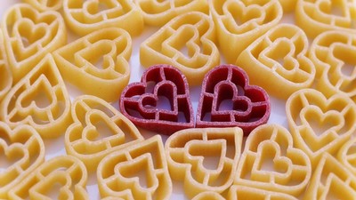 Hjerteformede pastastykker omgivet af traditionel fusilli-pasta med to røde hjerter i midten.