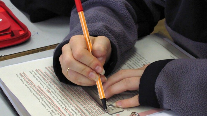 Person, die mit einem Bleistift auf ein Dokument schreibt, trägt einen Ring und einen Pullover.