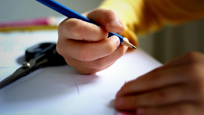 blauen Stift in der Hand. Weißes Papier liegt darunter. 